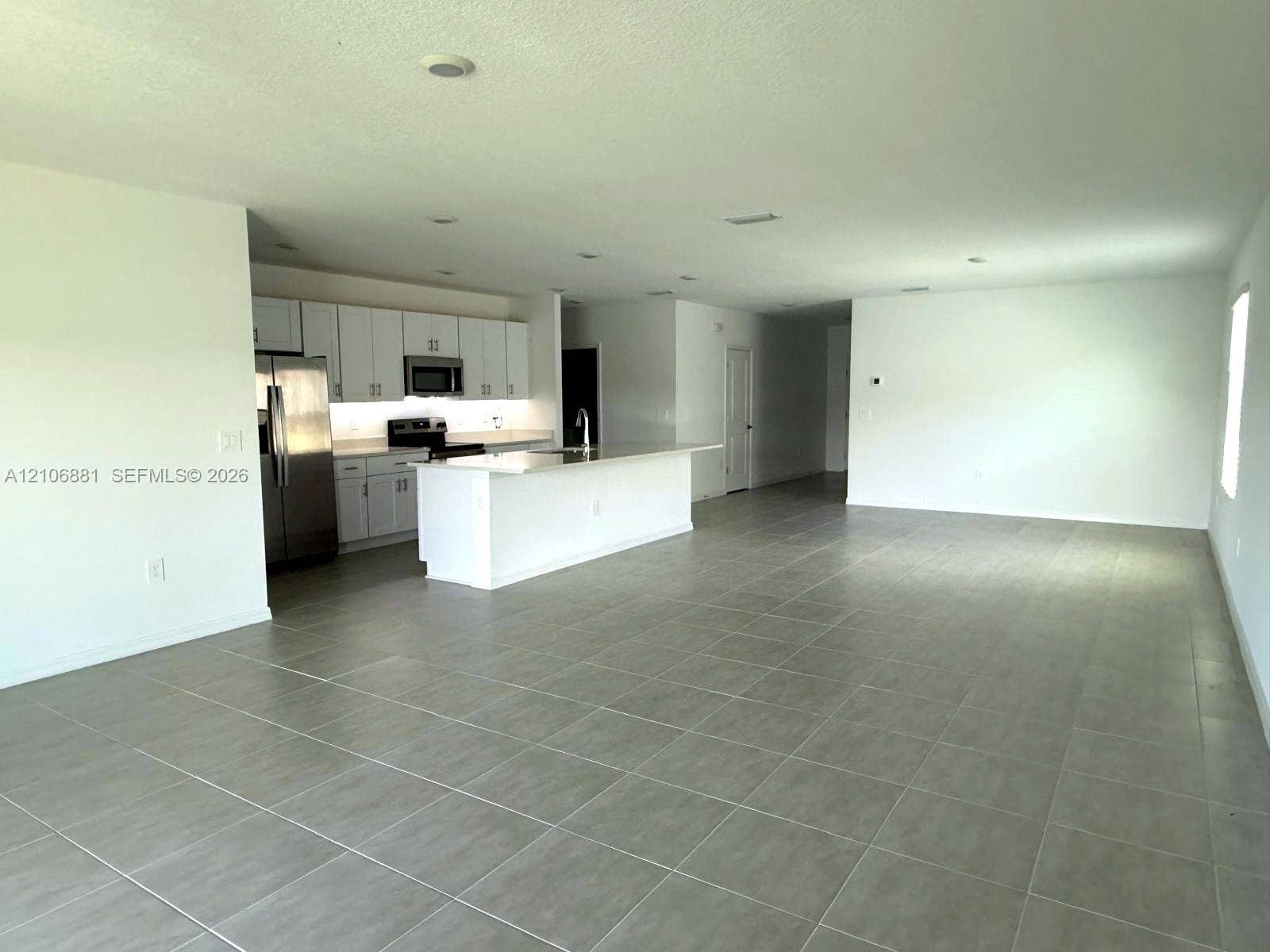 Open-concept space featuring large-format tile flooring, recessed lighting, and a kitchen equipped with white cabinetry, a stone-surface island, and stainless steel appliances