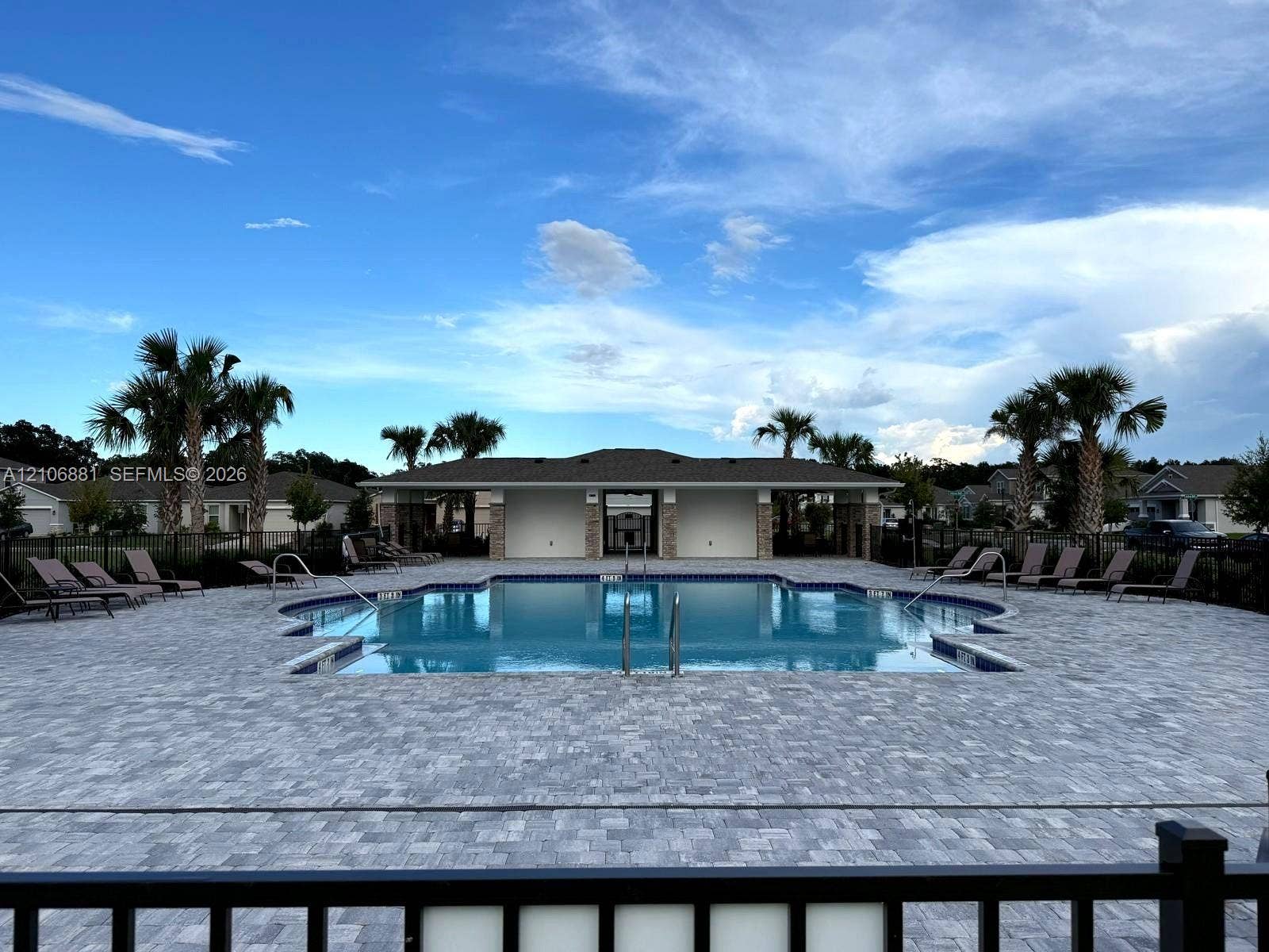 In-ground swimming pool featuring a decorative paver deck, metal fencing, and an open-air pavilion