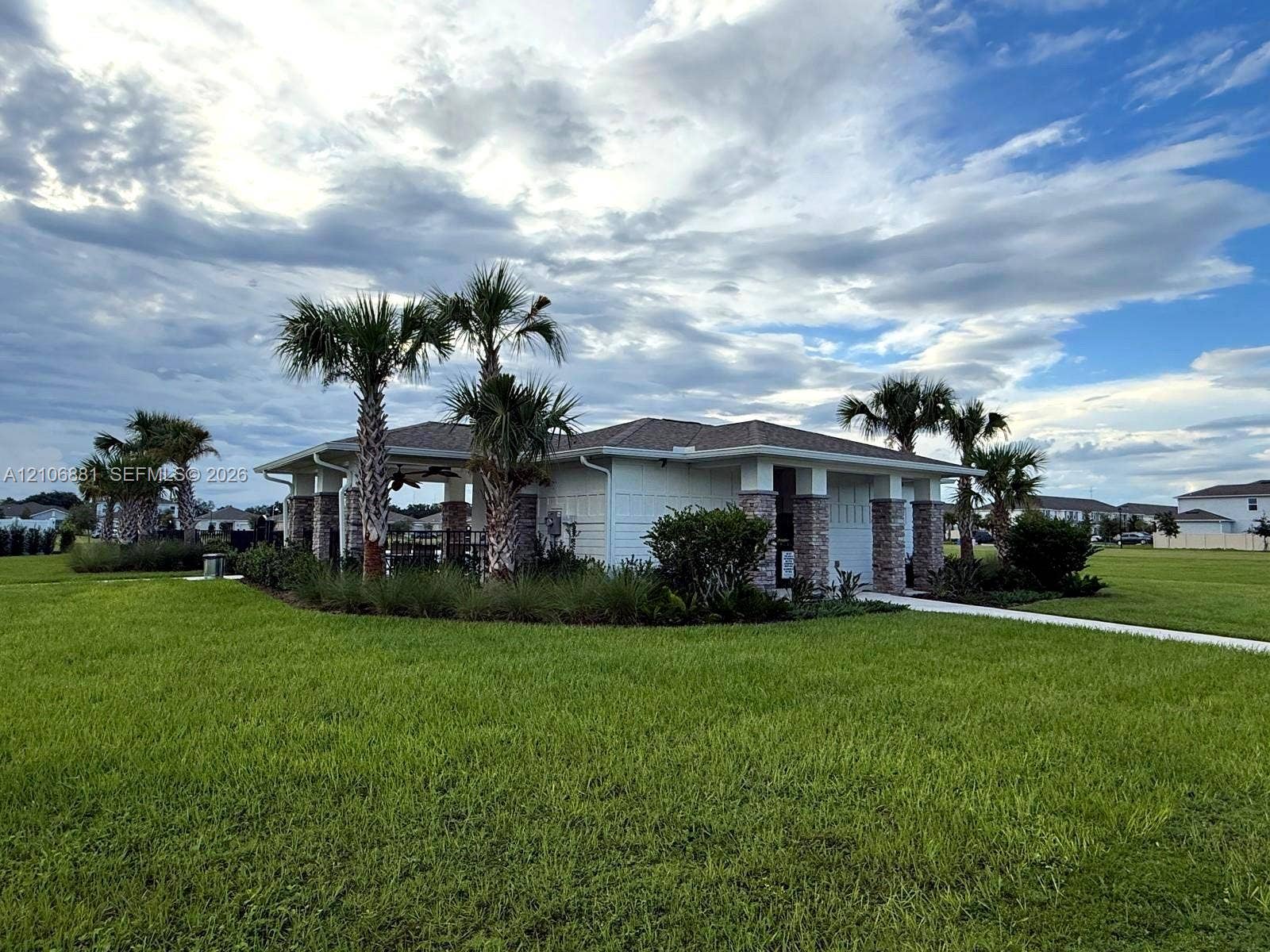 Pavilion featuring a shingle roof, stone-accented columns, white siding, and mature palm trees