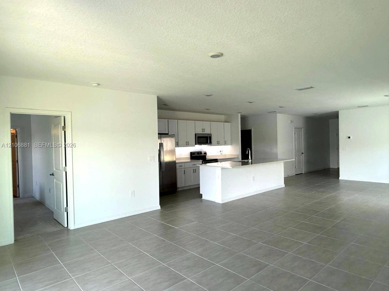 Open-concept kitchen featuring white shaker-style cabinetry, quartz countertops, a central island, and stainless steel appliances, all complemented by neutral tile flooring