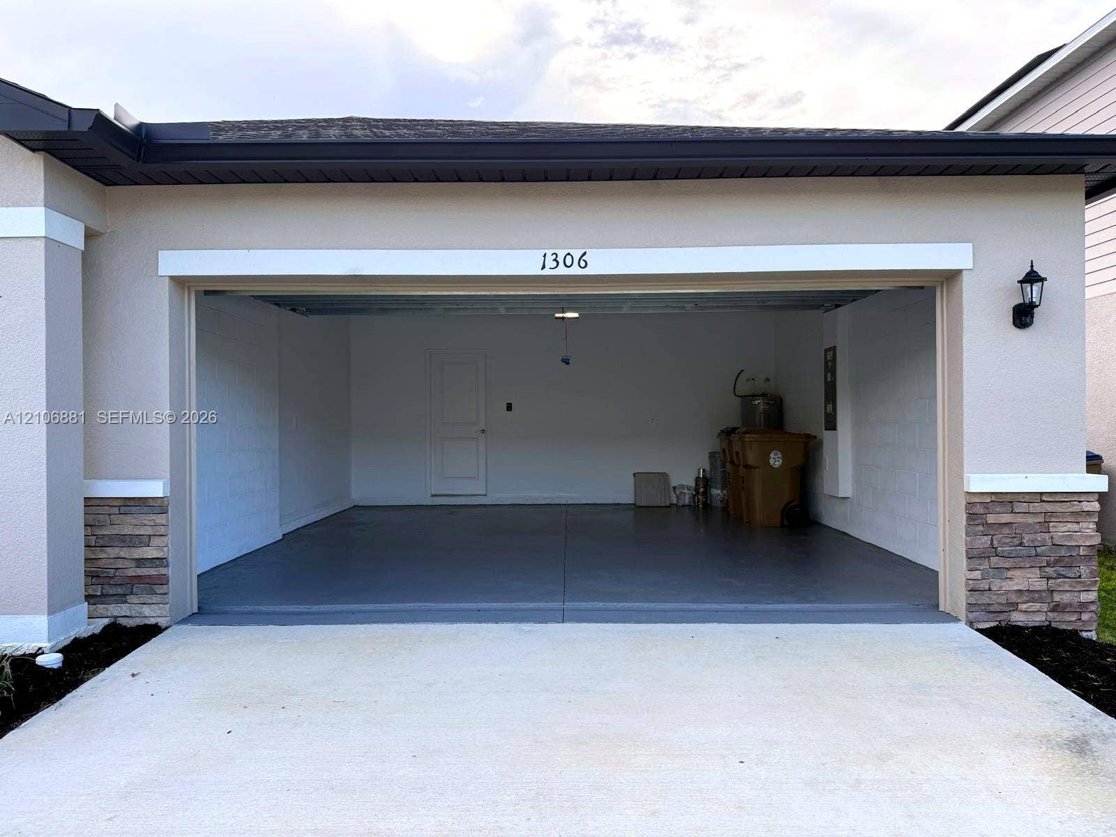 Two-car garage featuring finished concrete flooring, exterior stone veneer accents, and an attached wall-mounted lantern light