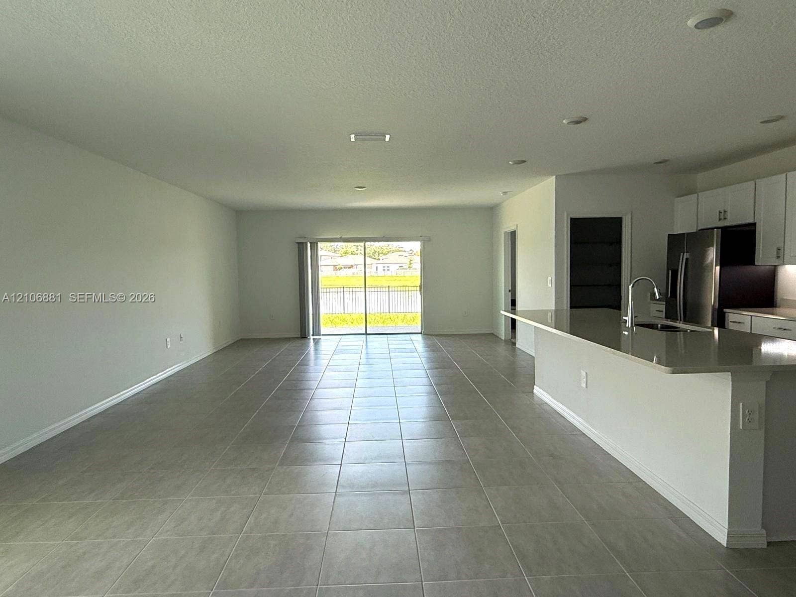 Open-concept interior featuring large-format neutral tile flooring, recessed ceiling lighting, a kitchen island with stone-surface countertops, stainless steel appliances, and sliding glass doors