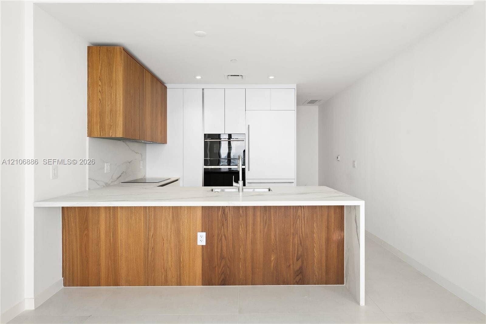 1400 Biscayne Boulevard, #2603, Miami, FL 33132 Kitchen featuring a center island with a stone-finish countertop and waterfall edge, two-tone wood-finish and flat-panel cabinetry, built-in wall oven, and integrated refrigerator