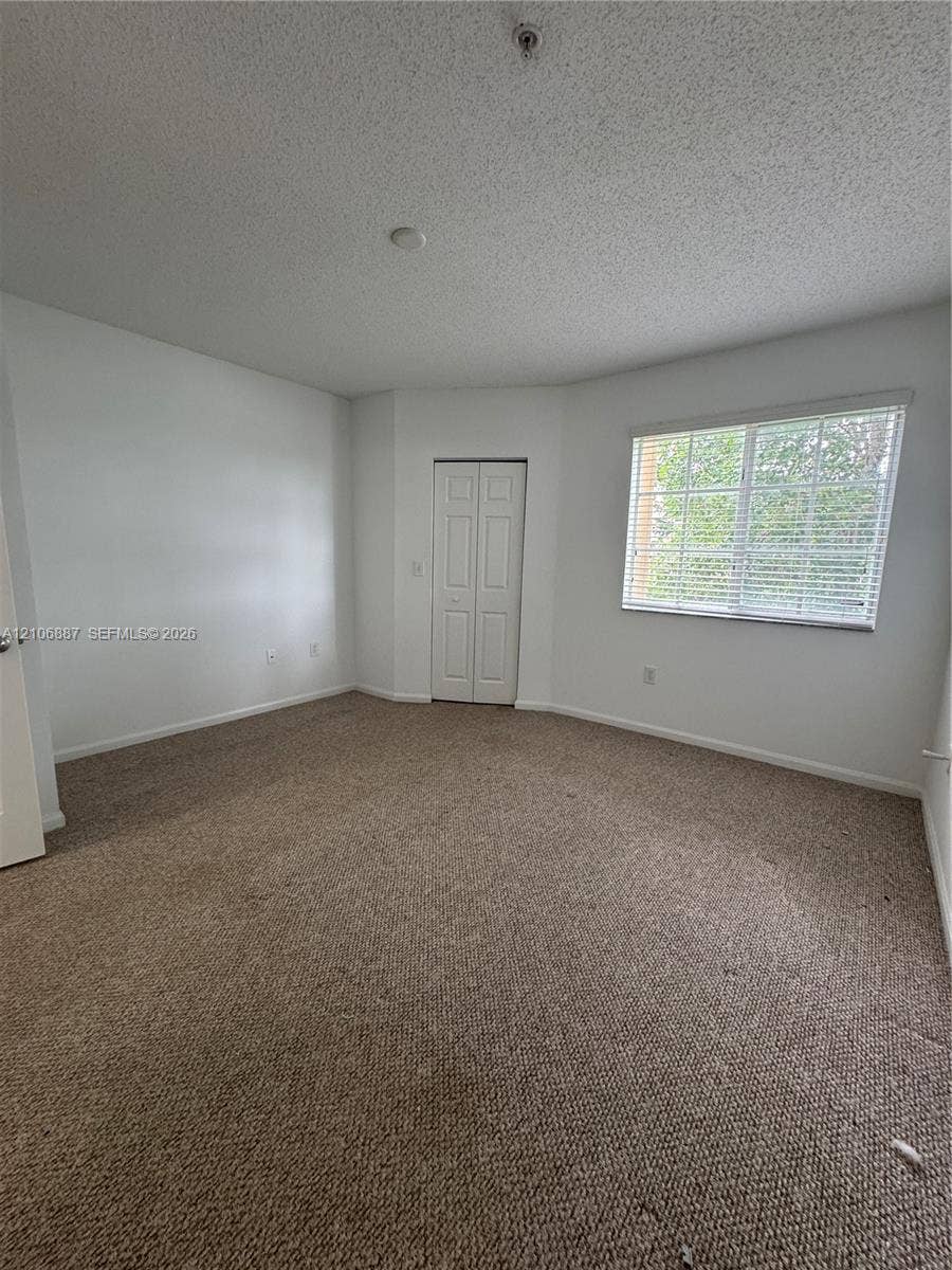7950 N Nob Hill Road, #202, Tamarac, Tamarac, FL 33321 Neutral-toned carpeting, textured ceiling, window with blinds, and dual-panel closet doors