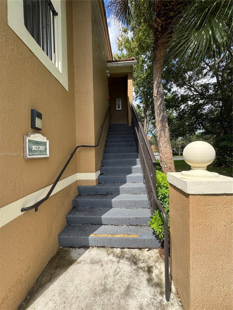 7950 N Nob Hill Road, #202, Tamarac, Tamarac, FL 33321 Stucco exterior featuring concrete stairs, a metal handrail, a decorative stone-finish address plaque, and a masonry pillar topped with a spherical finial
