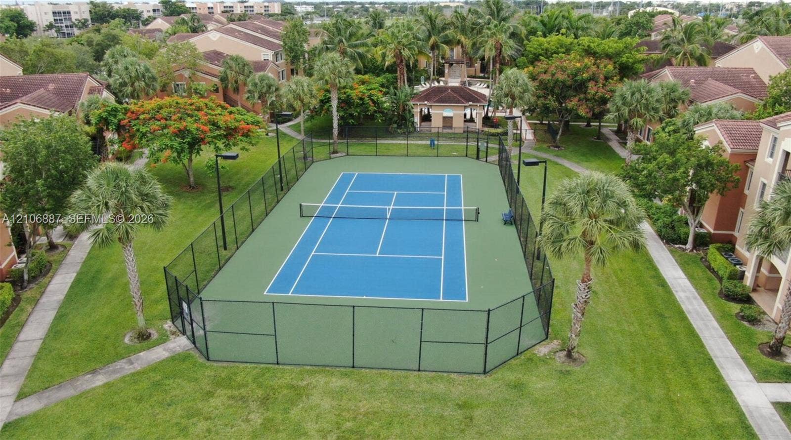 7950 N Nob Hill Road, #202, Tamarac, Tamarac, FL 33321 Tennis court featuring a paved surface, perimeter fencing, high-mast lighting, and surrounding landscaped grounds