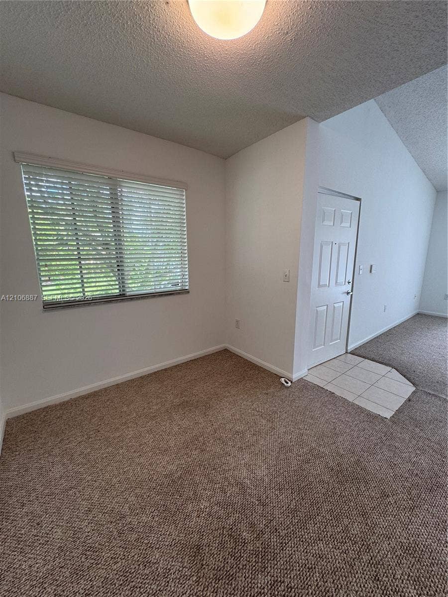 7950 N Nob Hill Road, #202, Tamarac, Tamarac, FL 33321 Interior area featuring vaulted ceilings, textured wall finishes, neutral carpeting, a tiled entryway, and horizontal window blinds