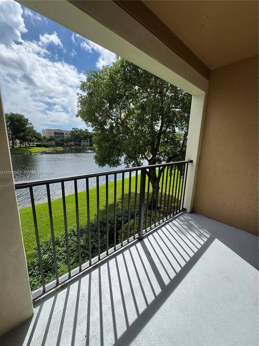 7950 N Nob Hill Road, #202, Tamarac, Tamarac, FL 33321 Covered balcony featuring a metal railing, concrete flooring, and water frontage with mature landscaping