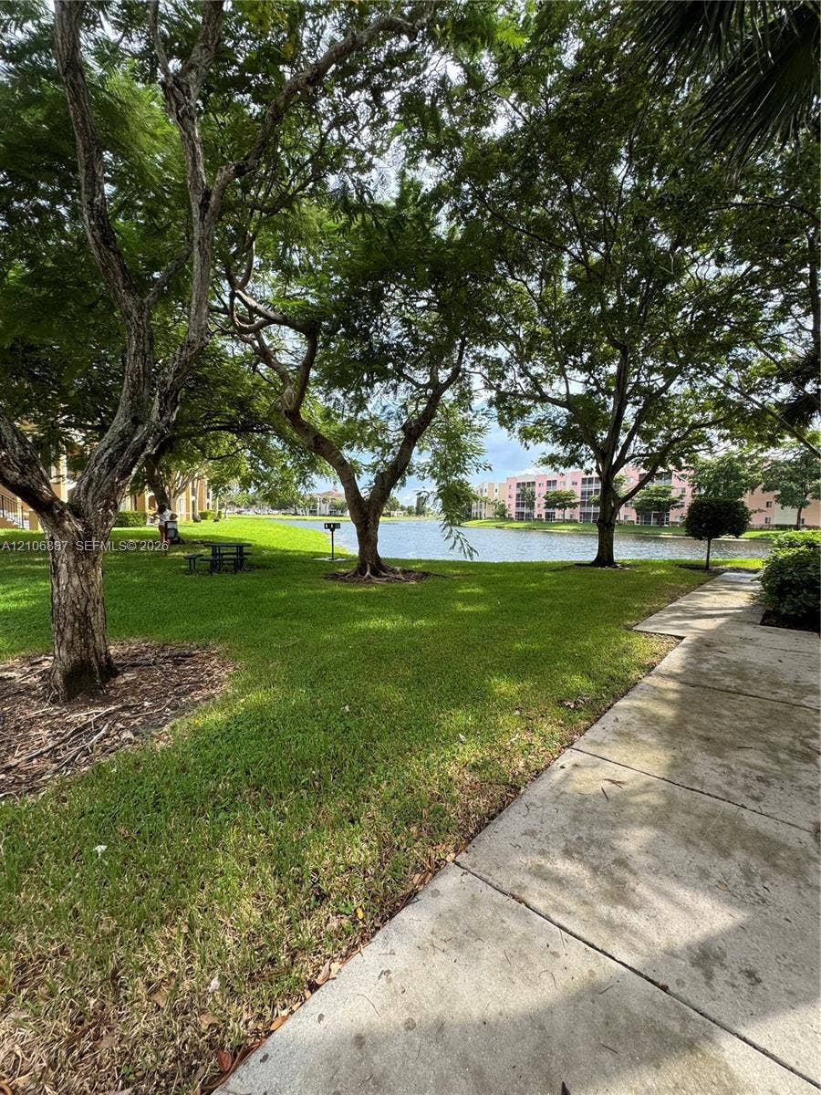 7950 N Nob Hill Road, #202, Tamarac, Tamarac, FL 33321 Grounds featuring mature shade trees, expansive grass lawn, concrete walkway, and waterfront exposure