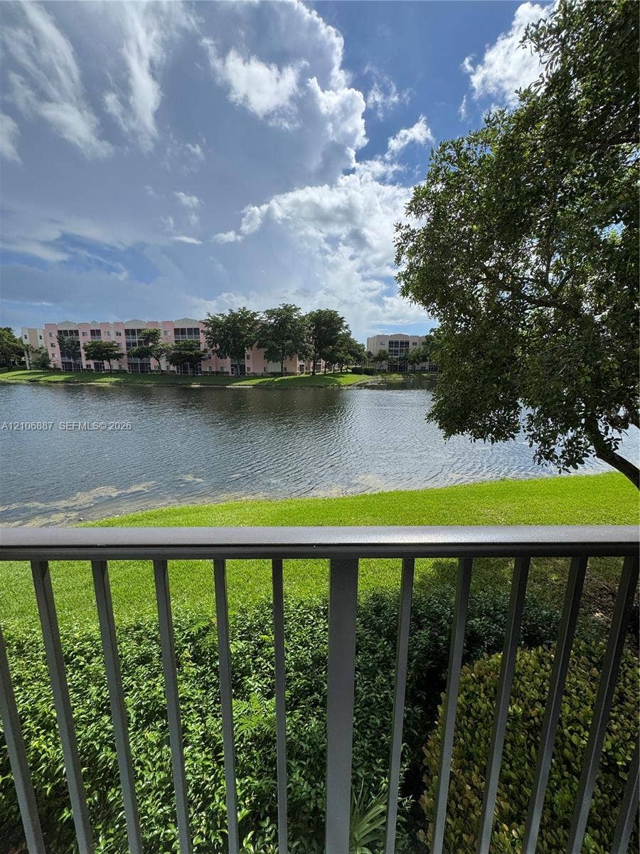 7950 N Nob Hill Road, #202, Tamarac, Tamarac, FL 33321 Metal balcony railing overlooking a lake, expansive grass lawn, and mature trees
