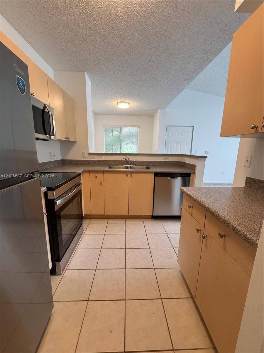 7950 N Nob Hill Road, #202, Tamarac, Tamarac, FL 33321 Kitchen featuring light-finish cabinetry, neutral stone-textured countertops, stainless steel appliances, and ceramic tile flooring