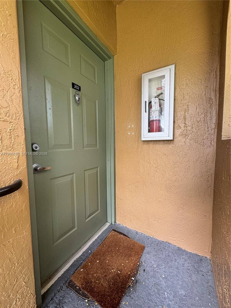 7950 N Nob Hill Road, #202, Tamarac, Tamarac, FL 33321 Solid core door featuring a polished metal lever handle, deadbolt lock, and recessed panel detailing, paired with a wall-mounted glass-enclosed fire extinguisher cabinet