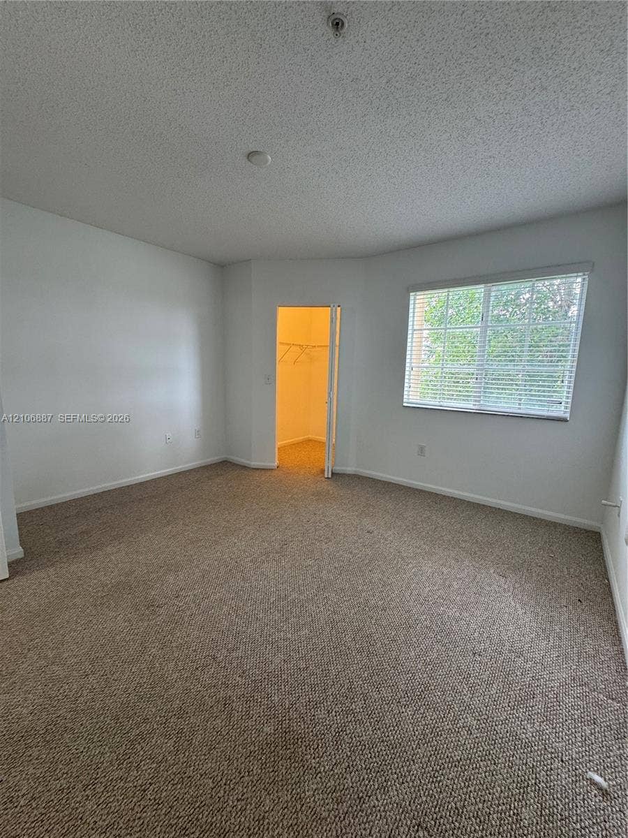 7950 N Nob Hill Road, #202, Tamarac, Tamarac, FL 33321 Room featuring neutral-toned carpeting, textured ceiling, a walk-in closet with built-in shelving, and a single window with horizontal blinds
