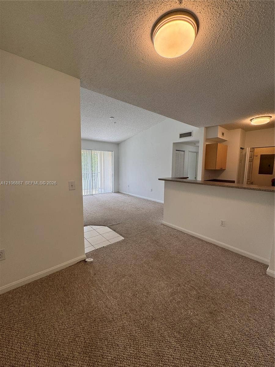 7950 N Nob Hill Road, #202, Tamarac, Tamarac, FL 33321 Interior space featuring neutral carpeting, a kitchen breakfast bar with countertop, tile entryway flooring, and sliding glass doors