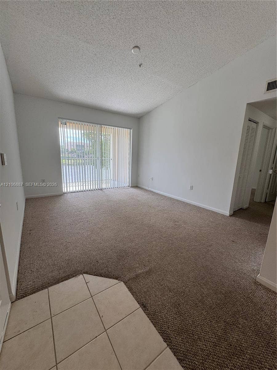 7950 N Nob Hill Road, #202, Tamarac, Tamarac, FL 33321 Living area featuring vaulted ceilings, neutral carpeting, sliding glass doors, and tiled flooring at the entry