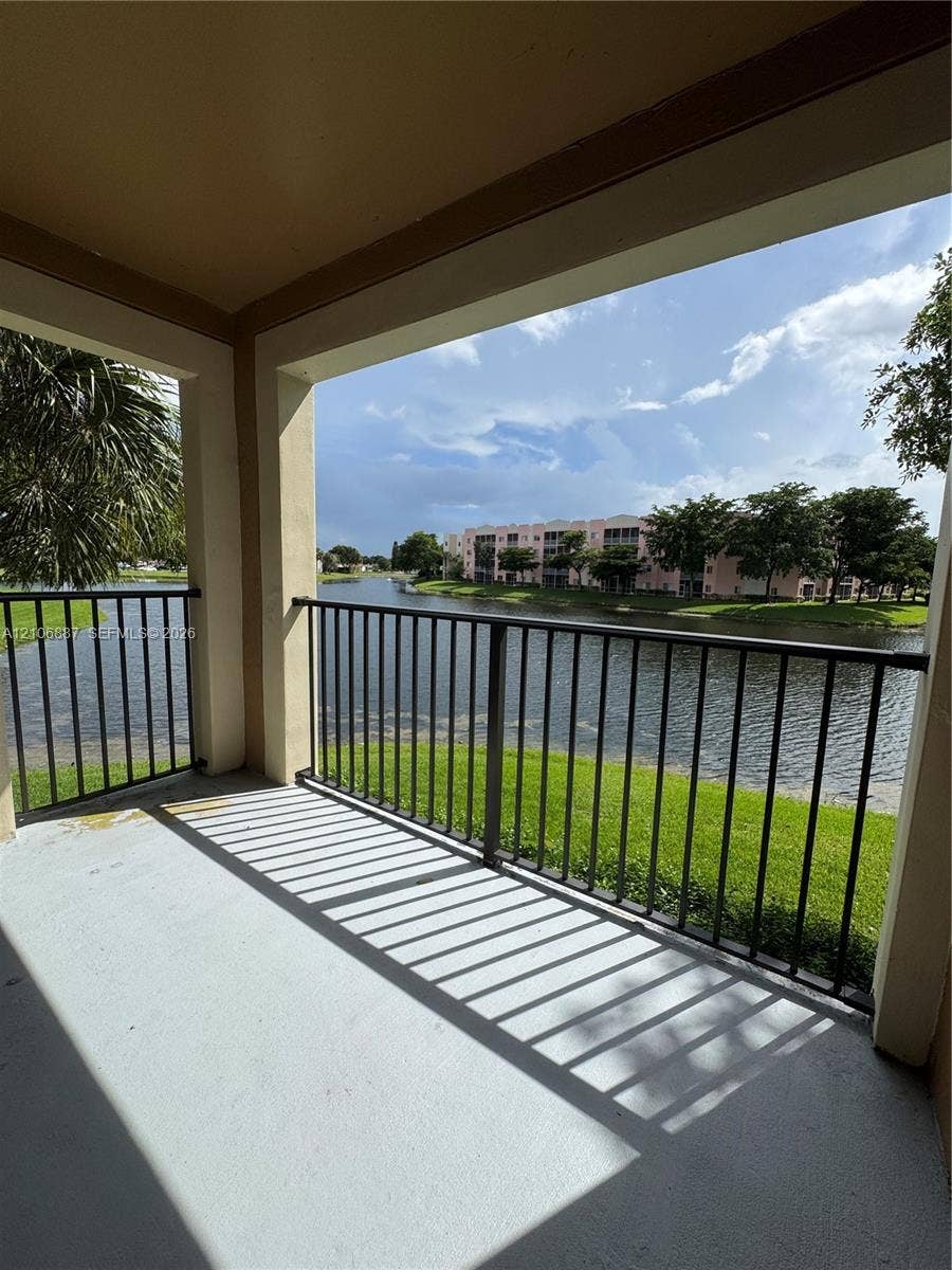 7950 N Nob Hill Road, #202, Tamarac, Tamarac, FL 33321 Covered balcony featuring concrete flooring and black metal railing, overlooking a water feature and landscaped grounds