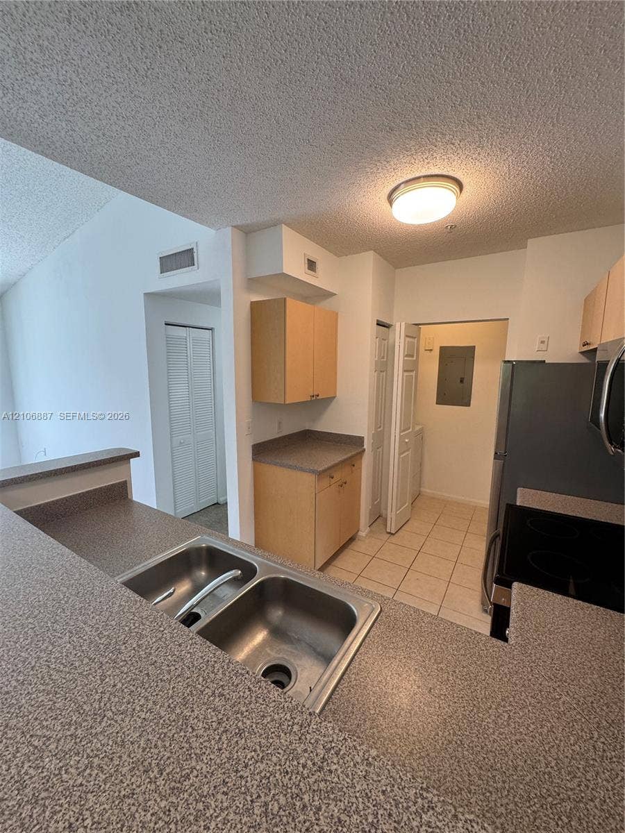 7950 N Nob Hill Road, #202, Tamarac, Tamarac, FL 33321 Kitchen featuring a dual-basin stainless steel sink, solid-surface countertops, light wood-finish cabinetry, and ceramic tile flooring