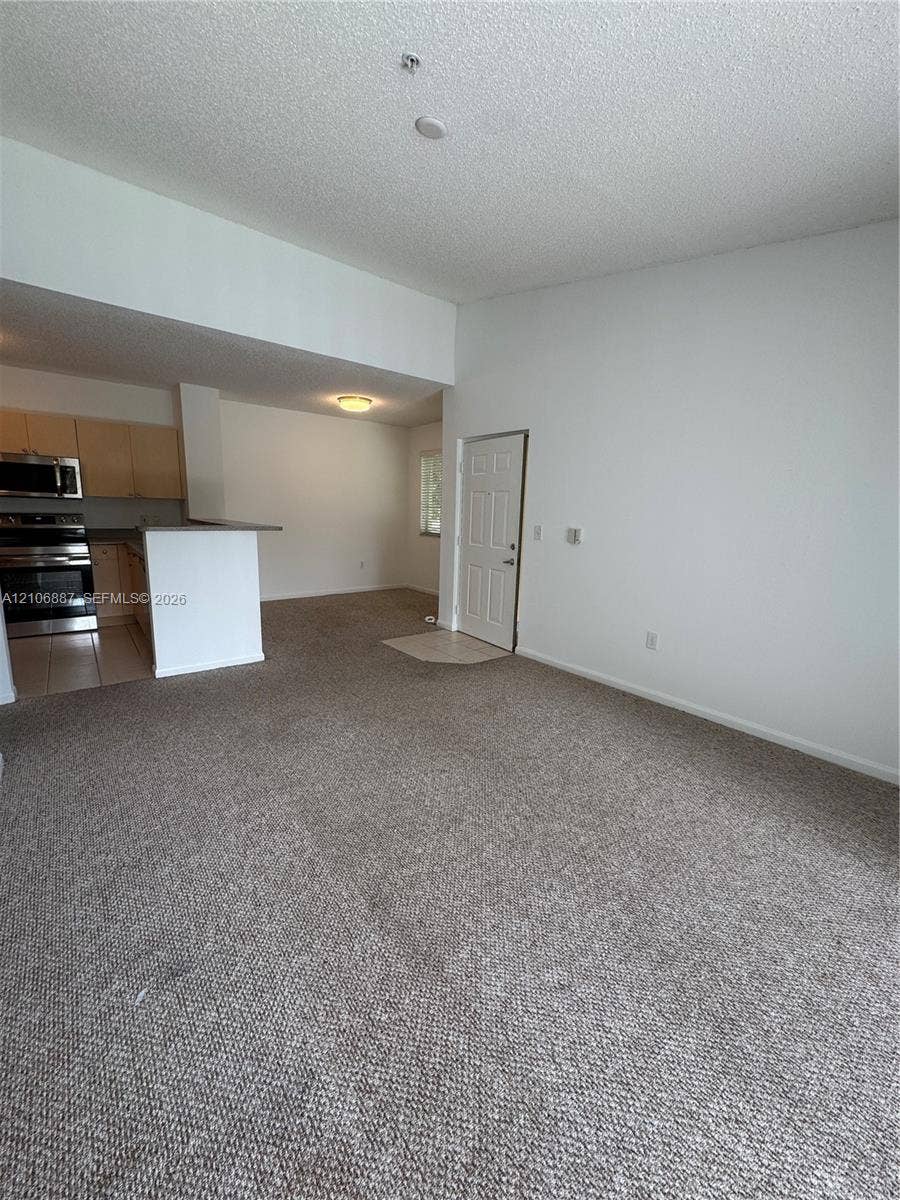 7950 N Nob Hill Road, #202, Tamarac, Tamarac, FL 33321 Open-concept interior featuring high vaulted ceilings, carpeted flooring, and a kitchen peninsula with integrated stainless steel appliances