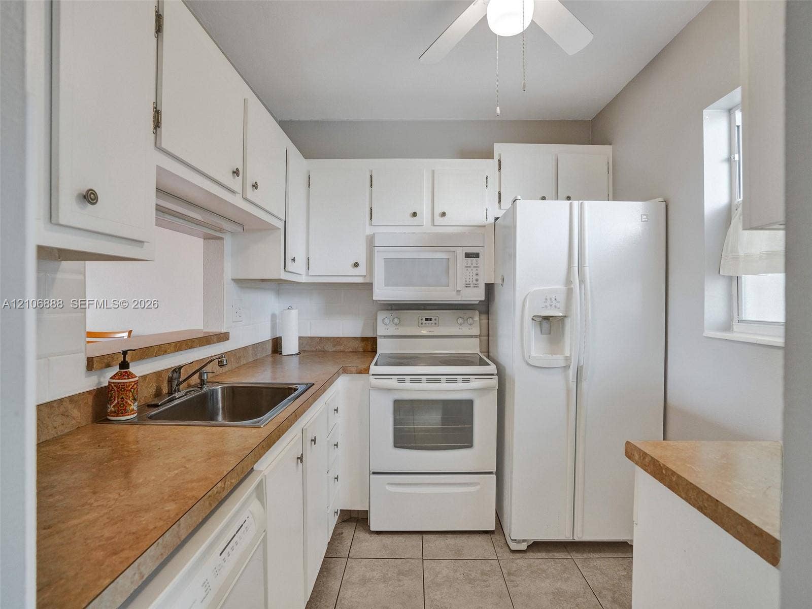 3506 NW 49th Avenue, #508, Lauderdale Lakes, FL 33319 Kitchen featuring white cabinetry, solid-surface countertops, tile flooring, and integrated white appliances including an over-the-range microwave
