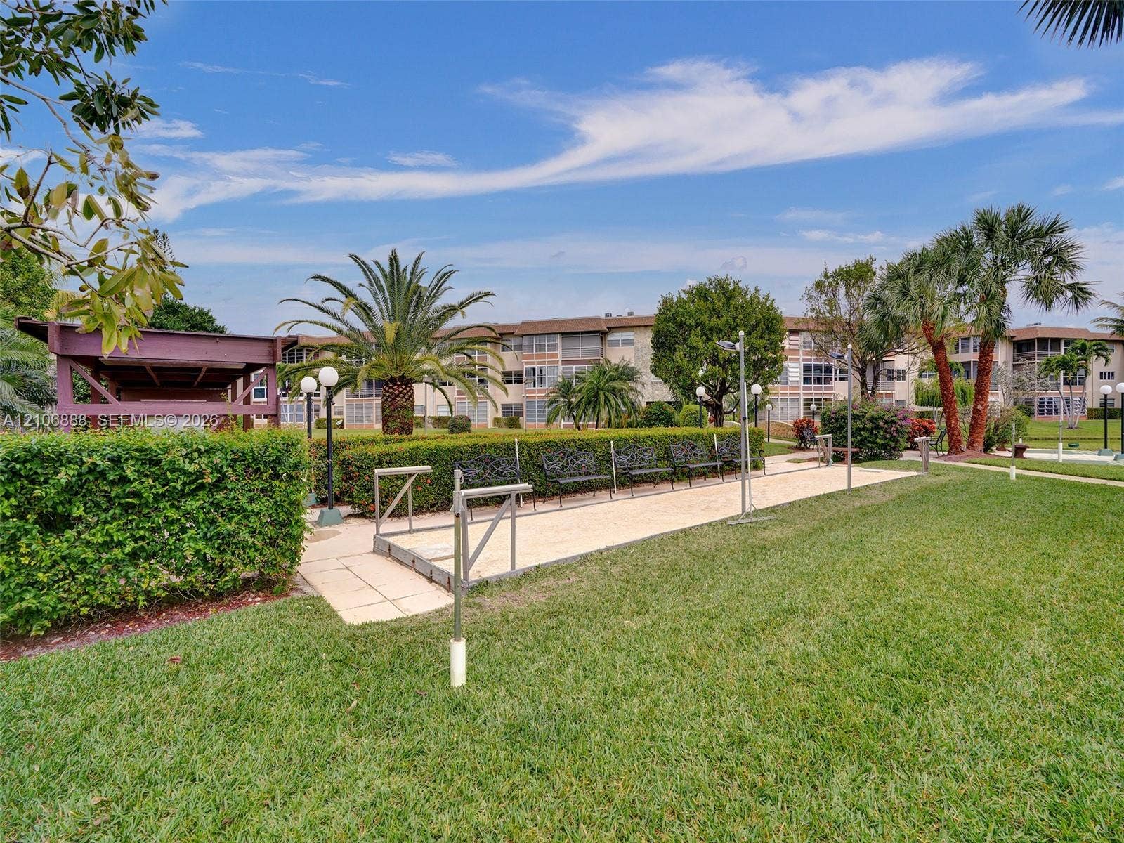 3506 NW 49th Avenue, #508, Lauderdale Lakes, FL 33319 Outdoor recreational space featuring a bocce ball court, manicured hedges, mature palm trees, and structural shaded pavilion