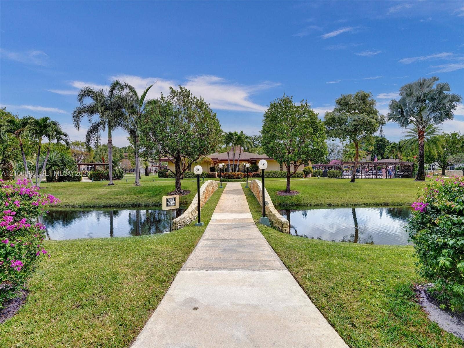 3506 NW 49th Avenue, #508, Lauderdale Lakes, FL 33319 Concrete walkway featuring a stone-clad bridge crossing a water feature, surrounded by manicured landscaping and mature trees