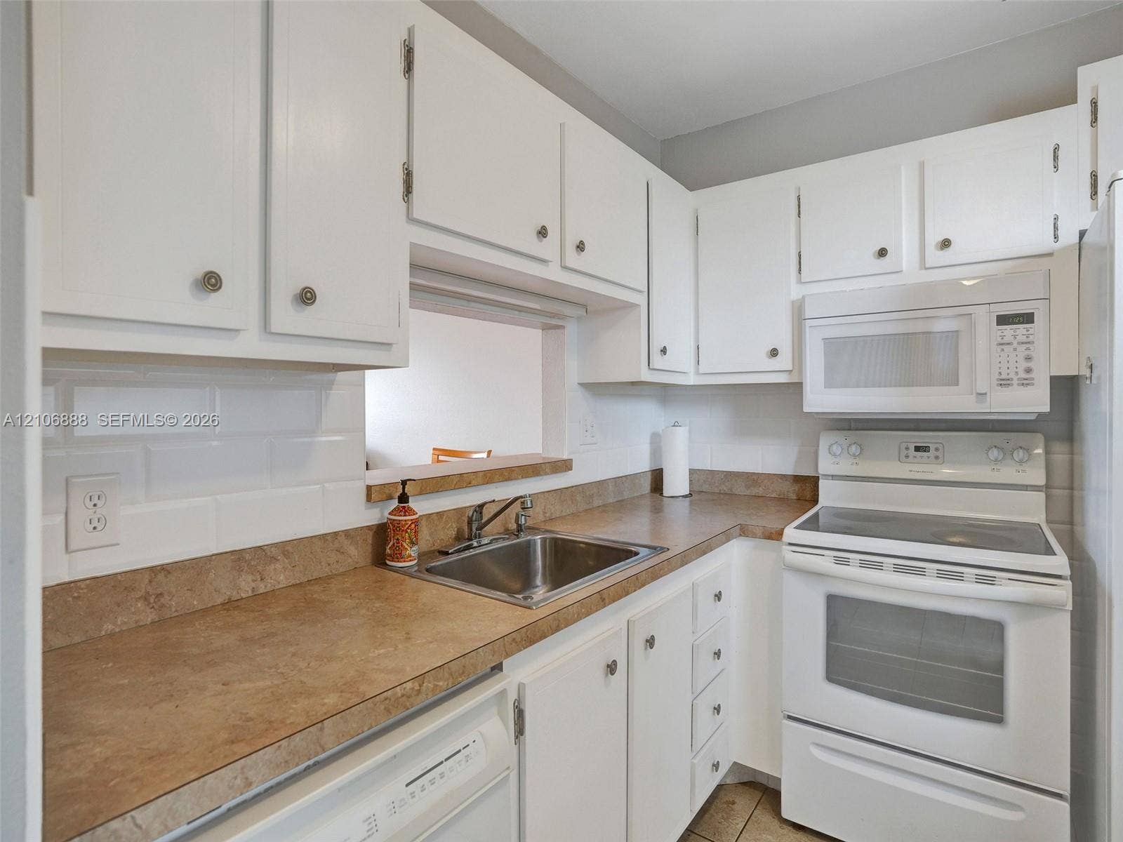 3506 NW 49th Avenue, #508, Lauderdale Lakes, FL 33319 Kitchen featuring white cabinetry, solid-surface countertops, white subway tile backsplash, stainless steel undermount sink, and white appliances