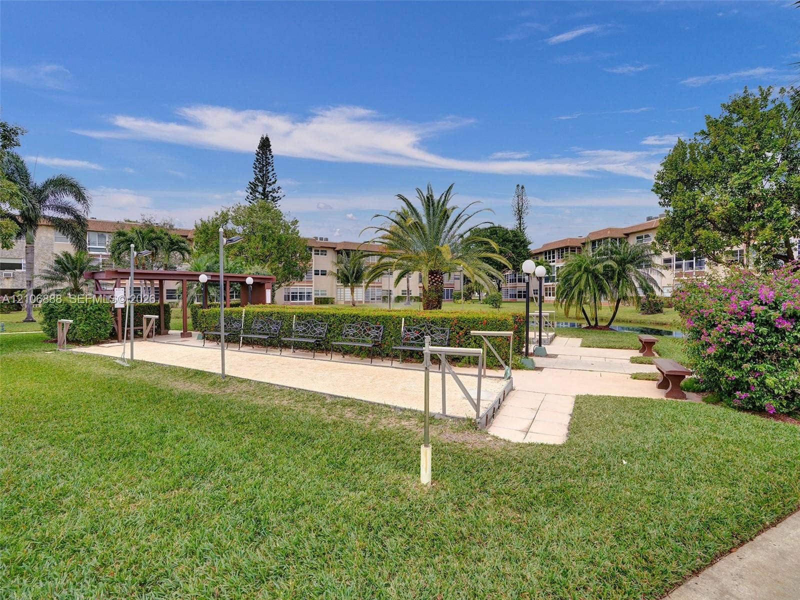3506 NW 49th Avenue, #508, Lauderdale Lakes, FL 33319 Common area featuring a bocce ball court, manicured lawn, sculpted hedges, ornamental palm trees, and permanent iron bench seating