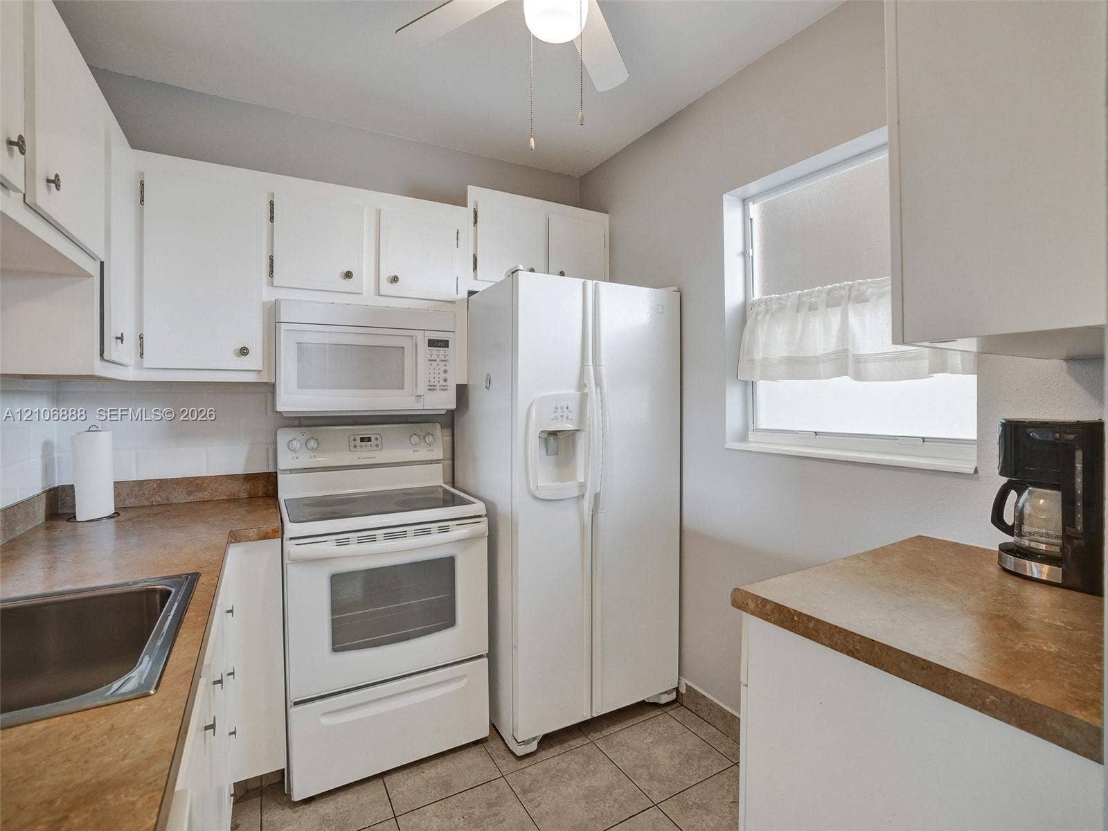 3506 NW 49th Avenue, #508, Lauderdale Lakes, FL 33319 Kitchen featuring white cabinetry, solid-surface countertops, tile flooring, an over-the-range microwave, and a white appliance suite