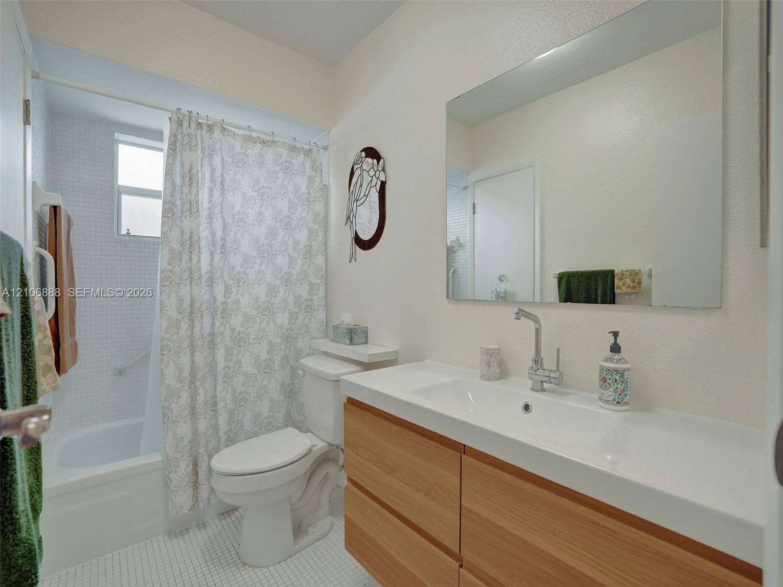 3506 NW 49th Avenue, #508, Lauderdale Lakes, FL 33319 Wall-mounted rectangular vanity with wood-finish cabinetry, integrated sink, chrome faucet, wall-spanning vanity mirror, and bathtub with full-height square tile surround