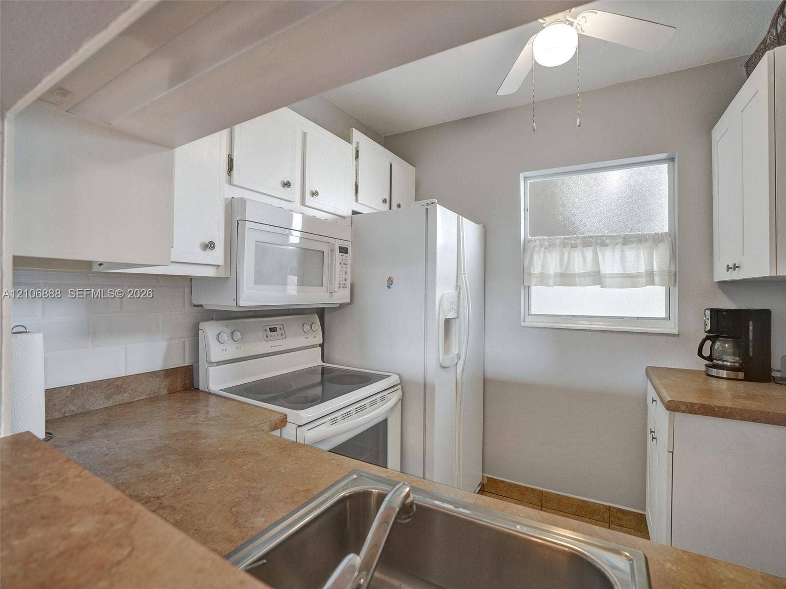 3506 NW 49th Avenue, #508, Lauderdale Lakes, FL 33319 Kitchen featuring white cabinetry, solid-surface countertops, subway tile backsplash, stainless steel sink, and white appliances