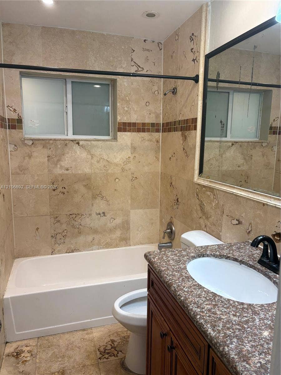 1322 N 31st Road, Hollywood, Hollywood, FL 33021 Bathroom featuring stone-tile wall surround with a decorative accent border, wood-finish vanity cabinet, speckled stone countertop with an undermount oval sink, and a framed mirror