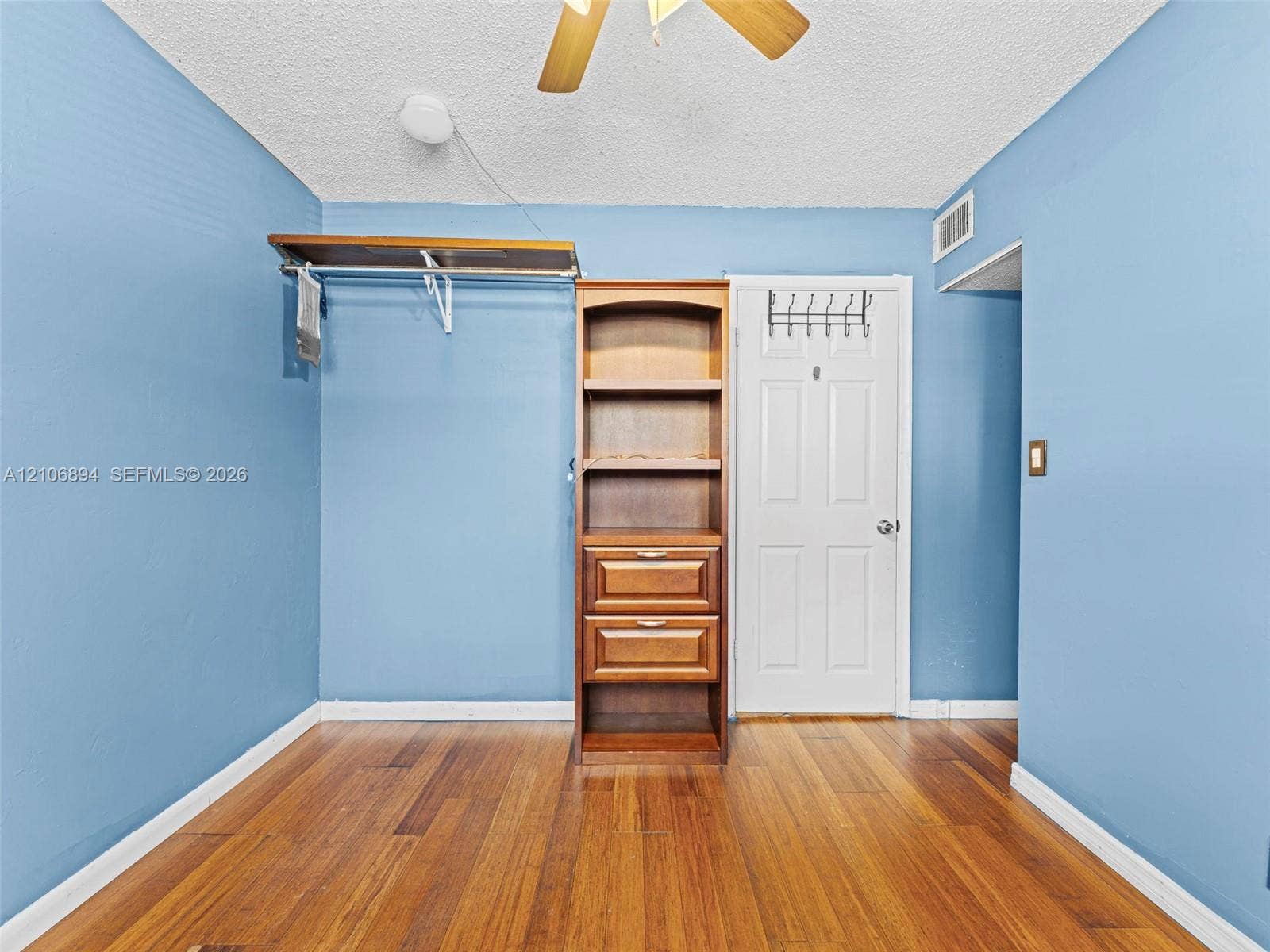 Room featuring wood-finish flooring, built-in wooden shelving with integrated drawers, wall-mounted garment shelving, a ceiling fan, and a six-panel door