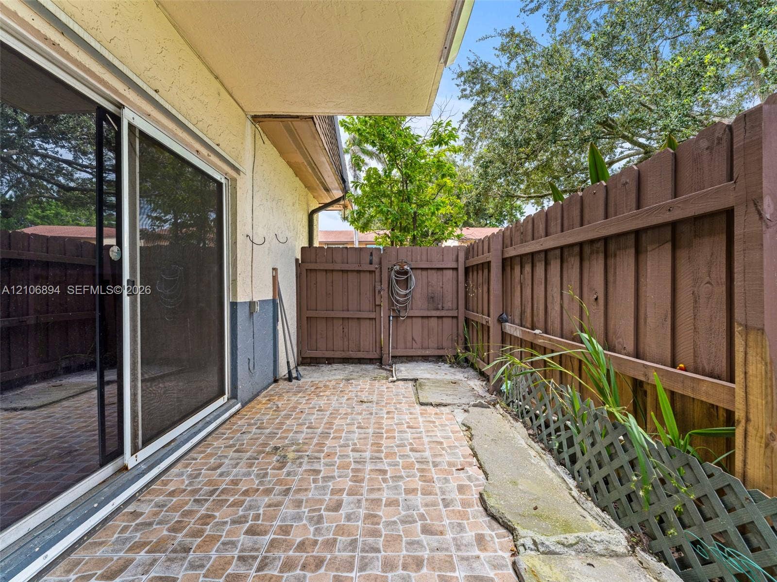 Covered patio featuring stone-patterned pavers and a fully enclosed wood-panel privacy fence