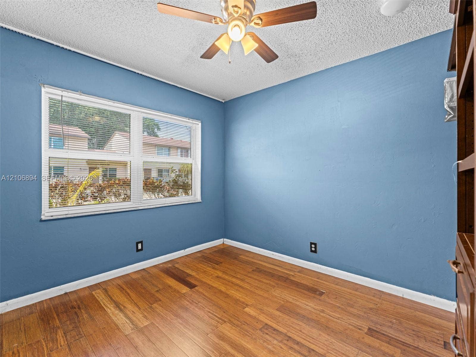 Room featuring wood-finish flooring, a multi-pane window with integrated blinds, and a ceiling-mounted light fixture with a fan
