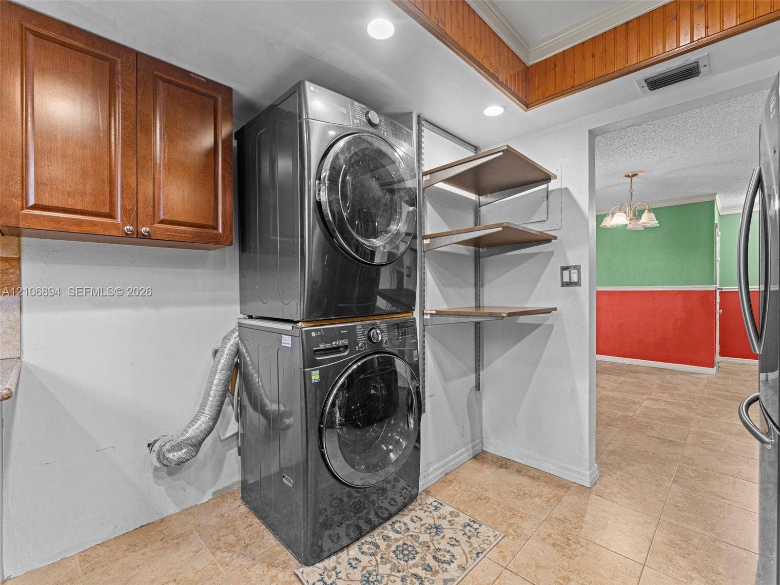 Laundry area featuring wood-finish wall cabinetry, adjustable metal shelving, and tile flooring