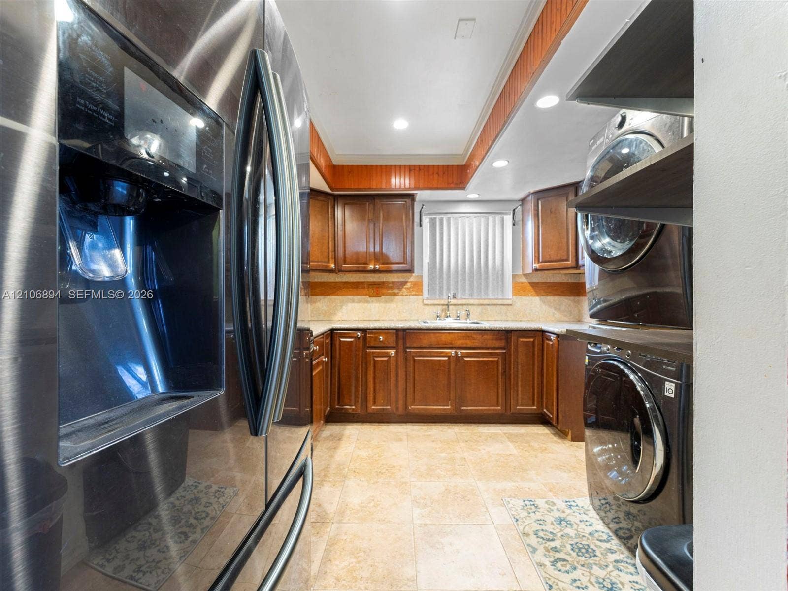 Wood cabinetry, stone-finish countertops, tiled flooring, recessed lighting, and integrated laundry appliances