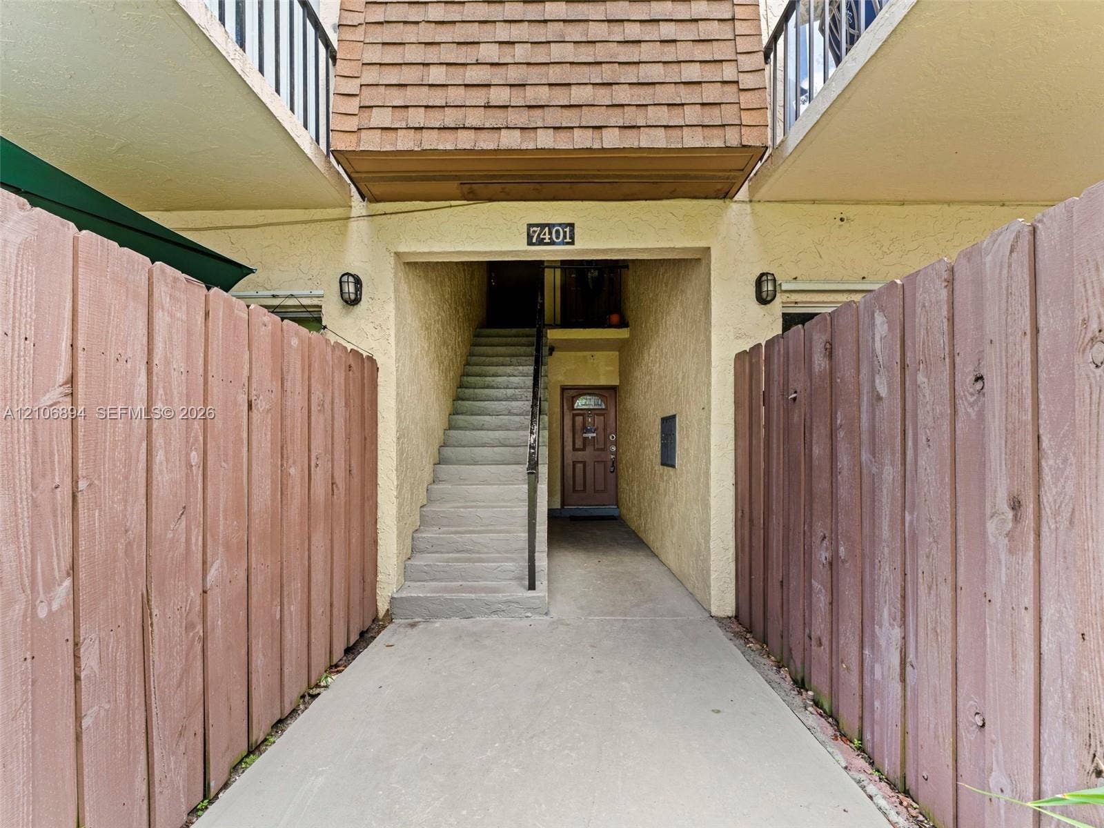 Exterior entry featuring a concrete staircase, wood-finish privacy fencing, and exterior wall-mounted light fixtures