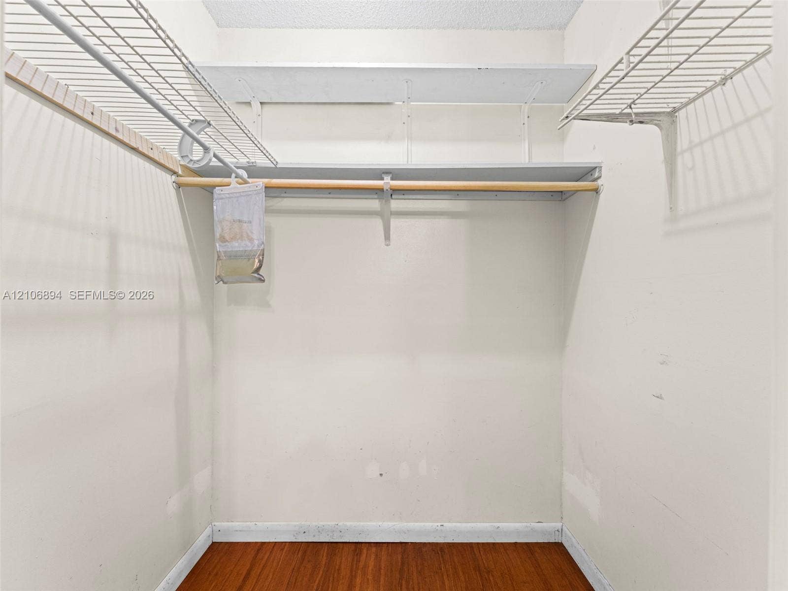 Walk-in storage space featuring wood-finish flooring and tiered wire shelving with integrated clothing rods