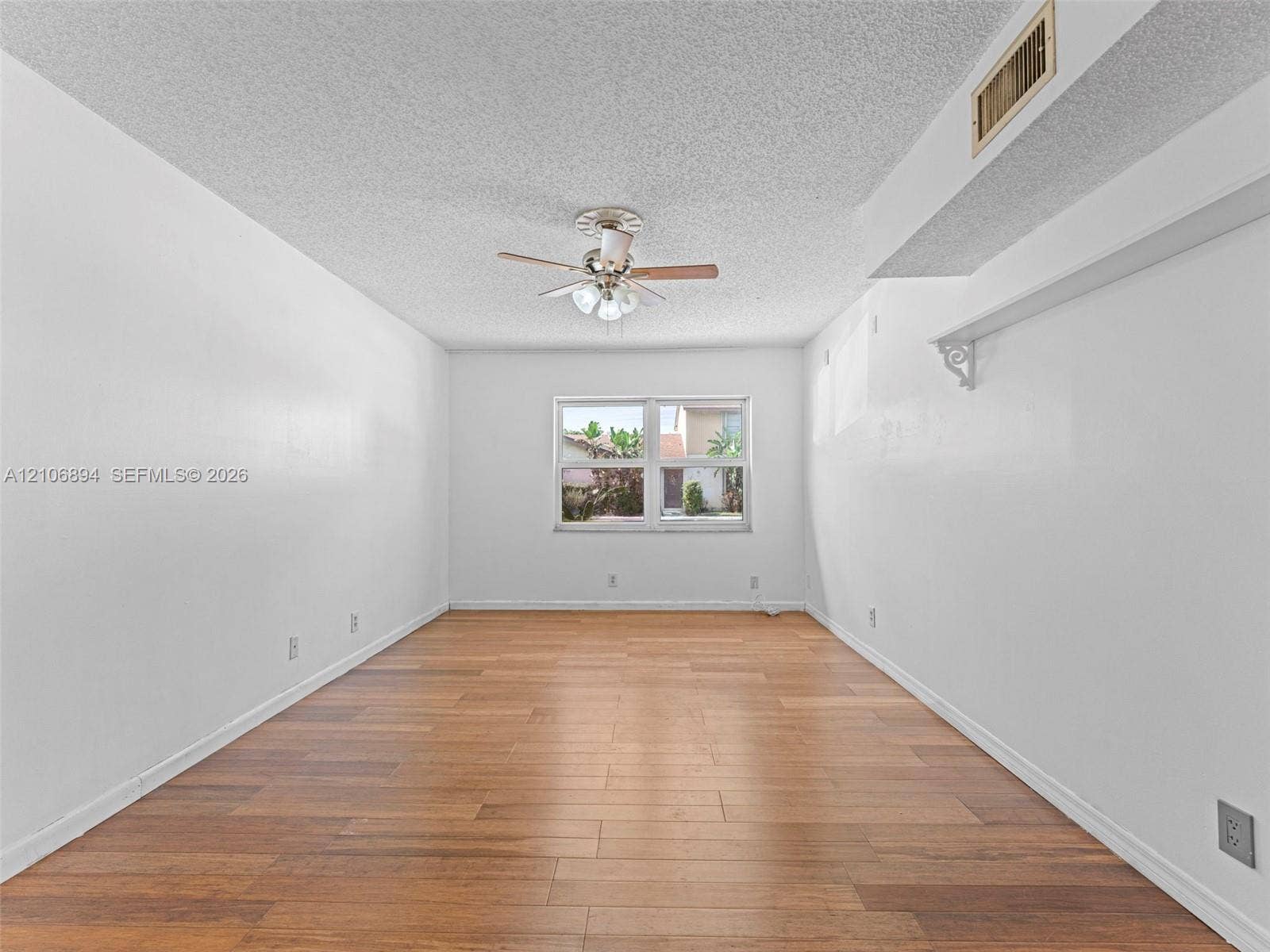 Interior space featuring wood-finish flooring, a ceiling fan with integrated lighting, and a wall-mounted decorative shelf