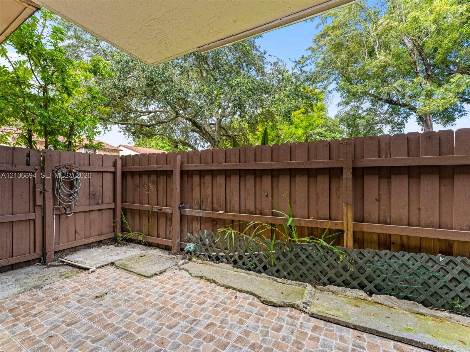 Patio area featuring stone-look paver flooring, stained wood privacy fencing, a decorative lattice screen, and an integrated gate