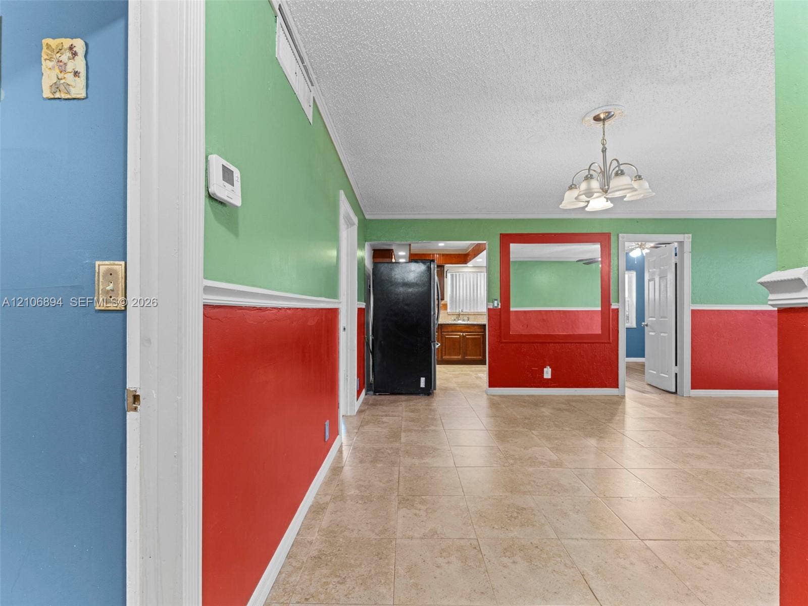 Tile flooring, multi-tone wall paint with chair rail molding, large wall-mounted mirror, and multi-arm chandelier lighting