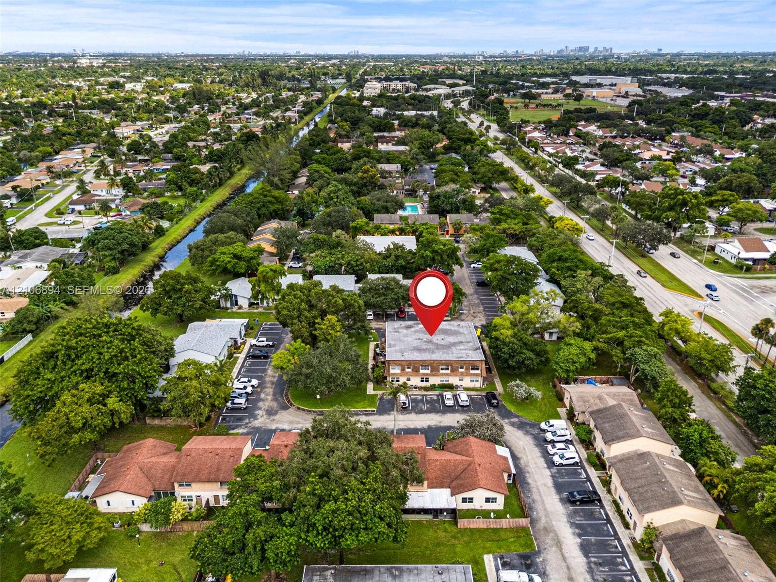 Aerial perspective of a multi-story residential building featuring a low-slope roof, brick-finish exterior, designated surface parking, and mature perimeter landscaping