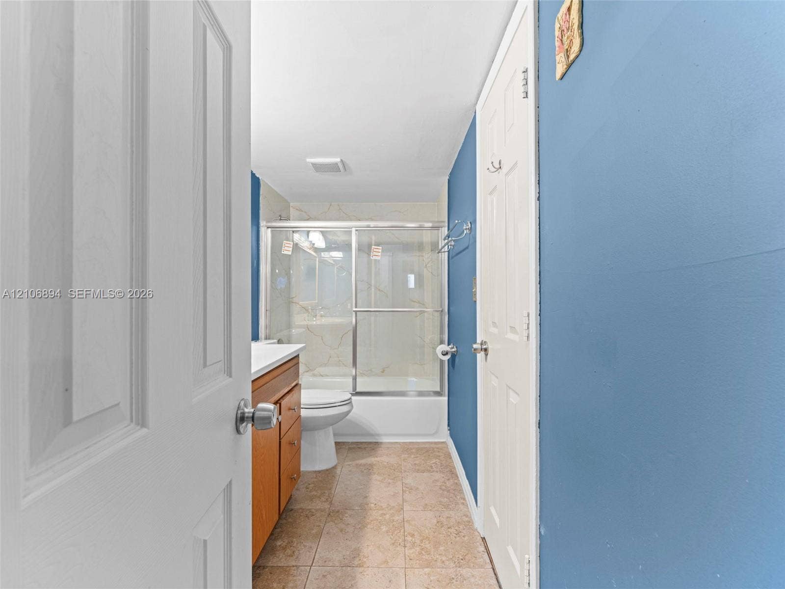 Bathroom featuring ceramic tile flooring, a wood-finish vanity cabinet, a tub-shower combination with a sliding glass door enclosure, and a built-in towel rack