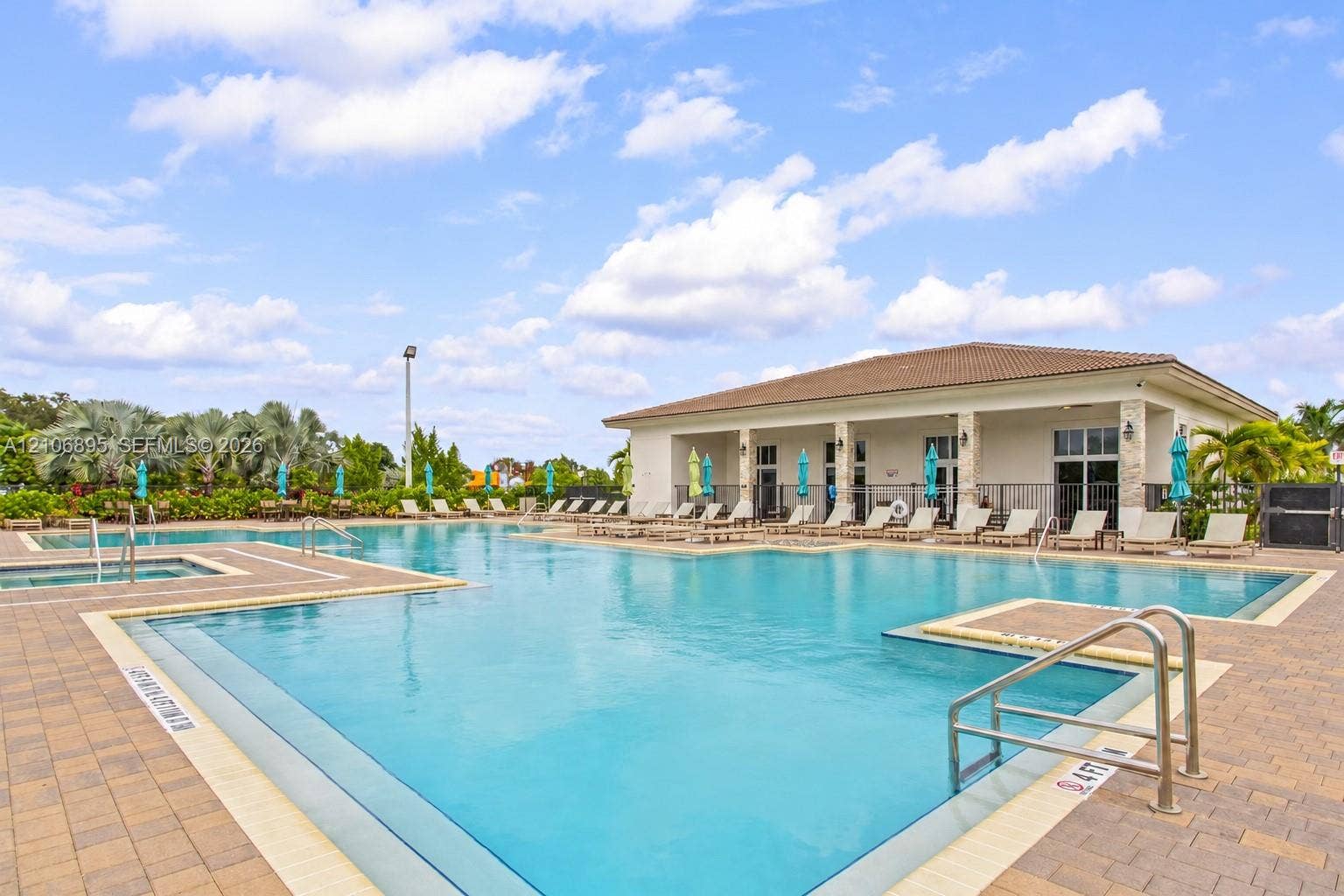 Resort-style swimming pool featuring paver decking, integrated spa, and a covered clubhouse pavilion