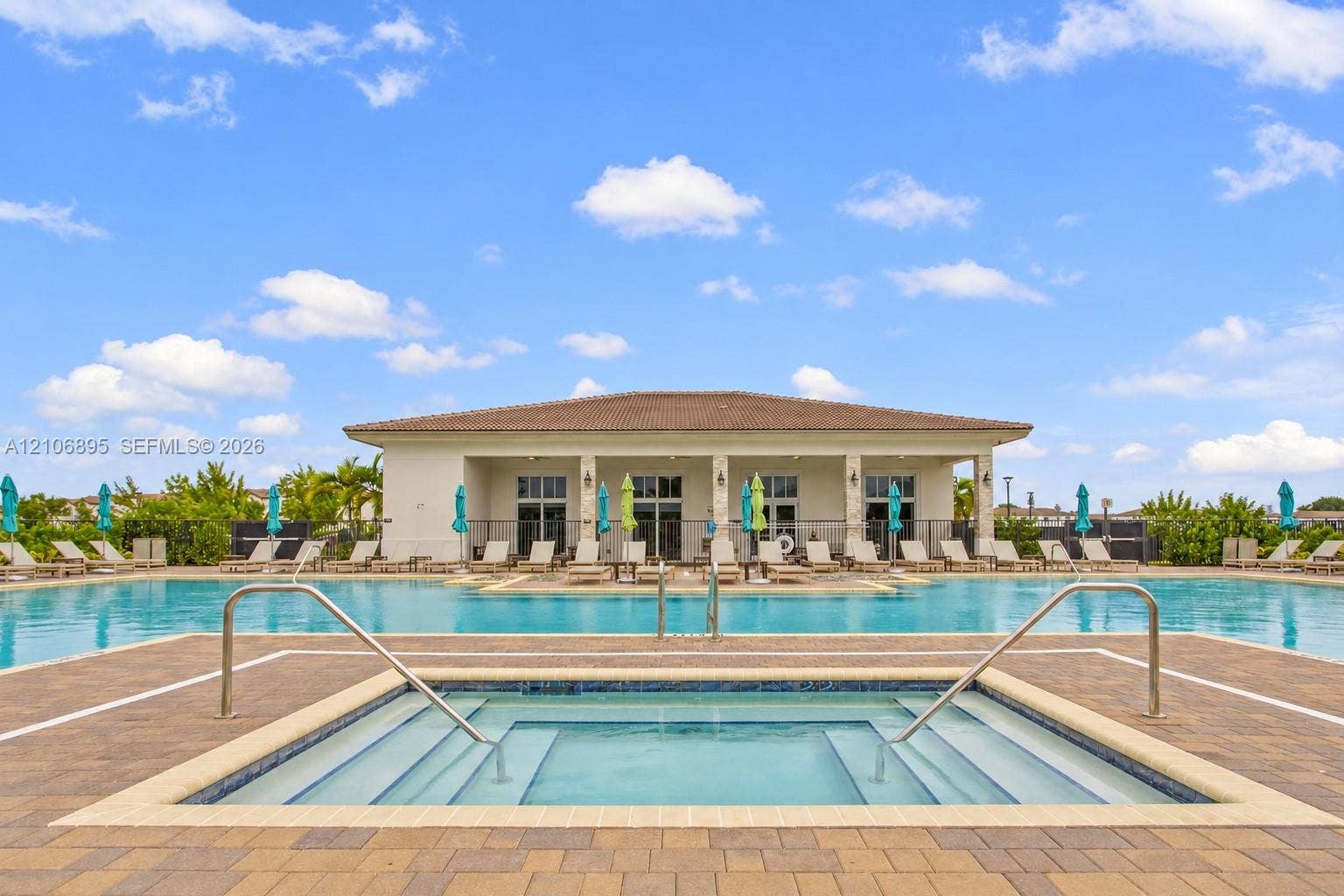 In-ground swimming pool and spa featuring paver decking, tiled borders, and metal handrails