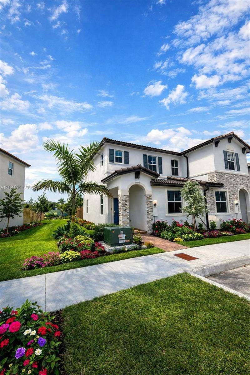 Two-story exterior featuring light-toned stucco finish, decorative stone veneer accents, multi-pane windows with shutters, and a covered entryway