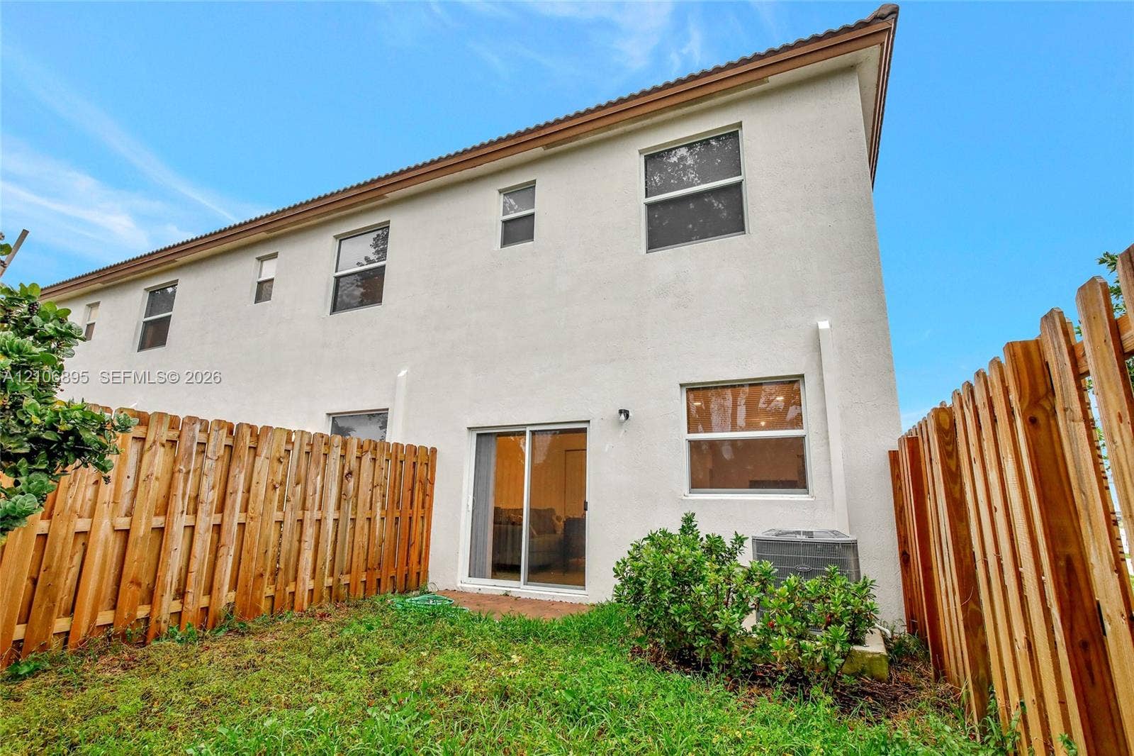 Stucco exterior with sliding glass doors, horizontal wood fencing, and a tiled roofline