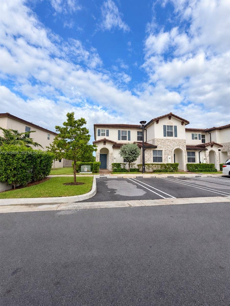 Stucco exterior with stone veneer accents, arched entryways, tiled roof, and dedicated surface parking