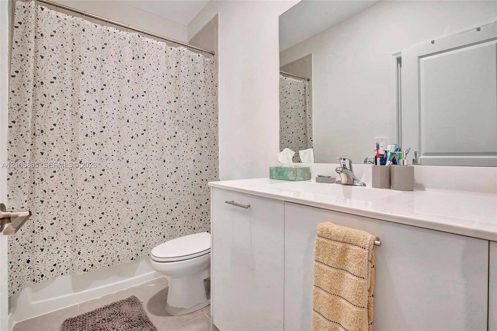 White vanity with an integrated countertop, polished chrome faucet, expansive wall-mounted mirror, and a porcelain toilet