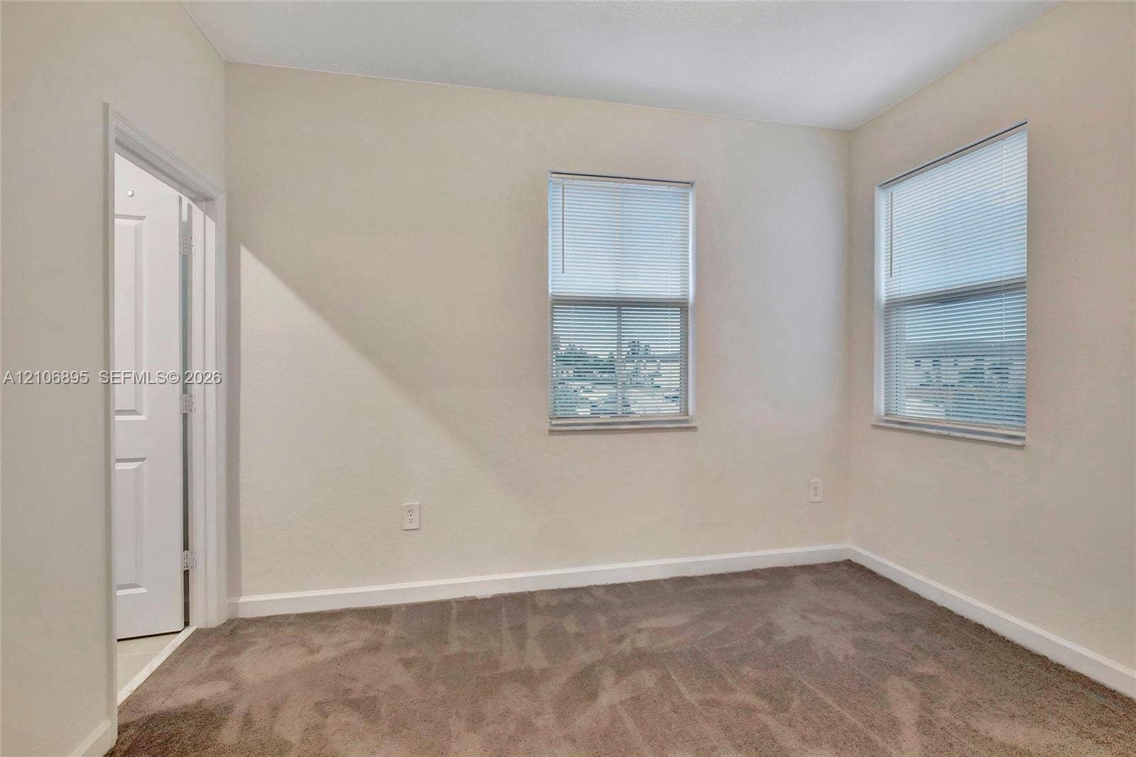 Neutral interior space featuring carpeted flooring, two windows with integrated blinds, and a single-panel interior door